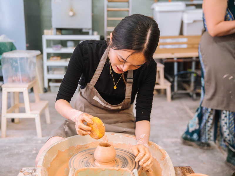 Woman holding a sponge spinning clay on the wheel